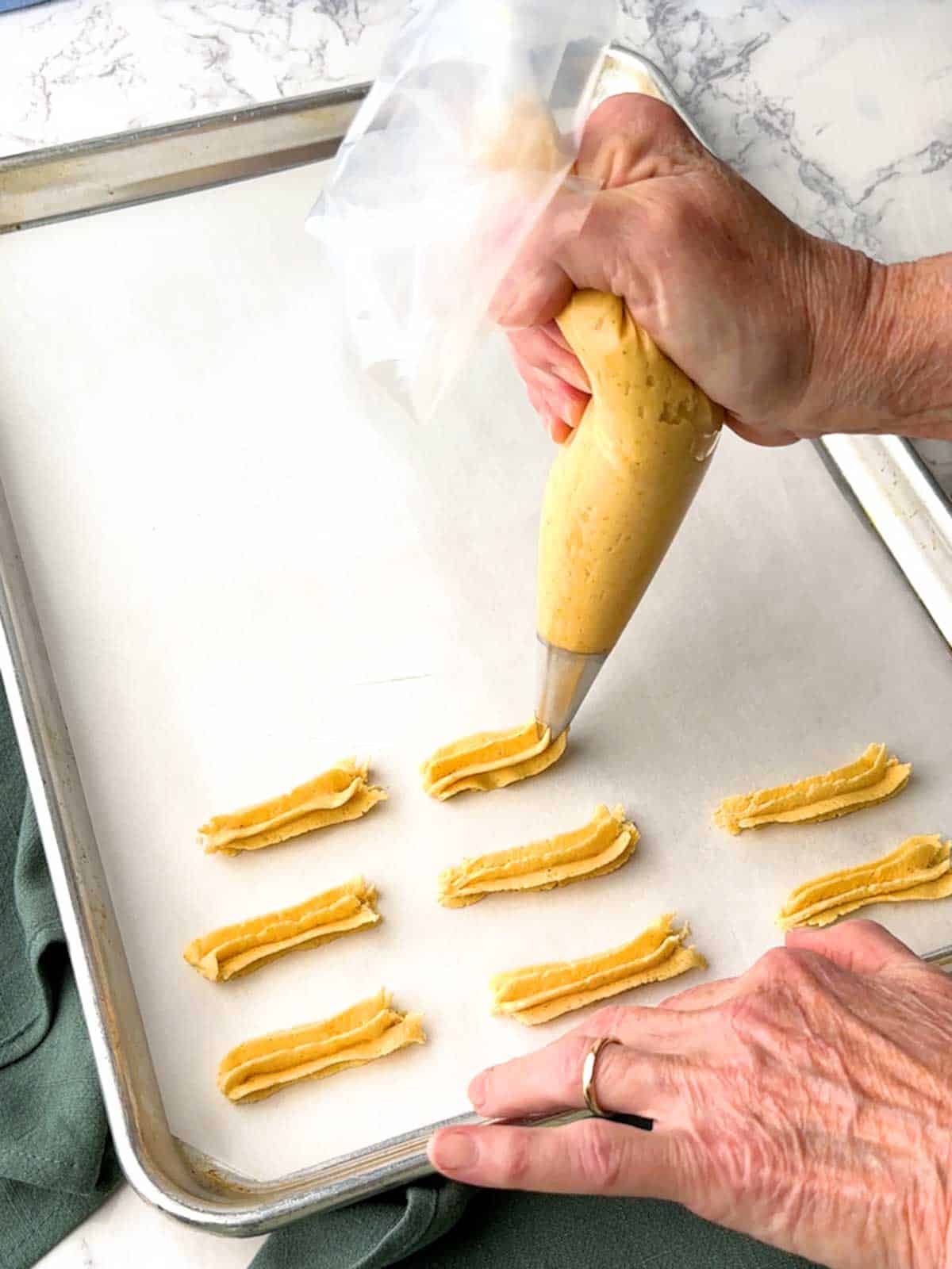 Piping the cheese straws onto a parchment-lined baking sheet.