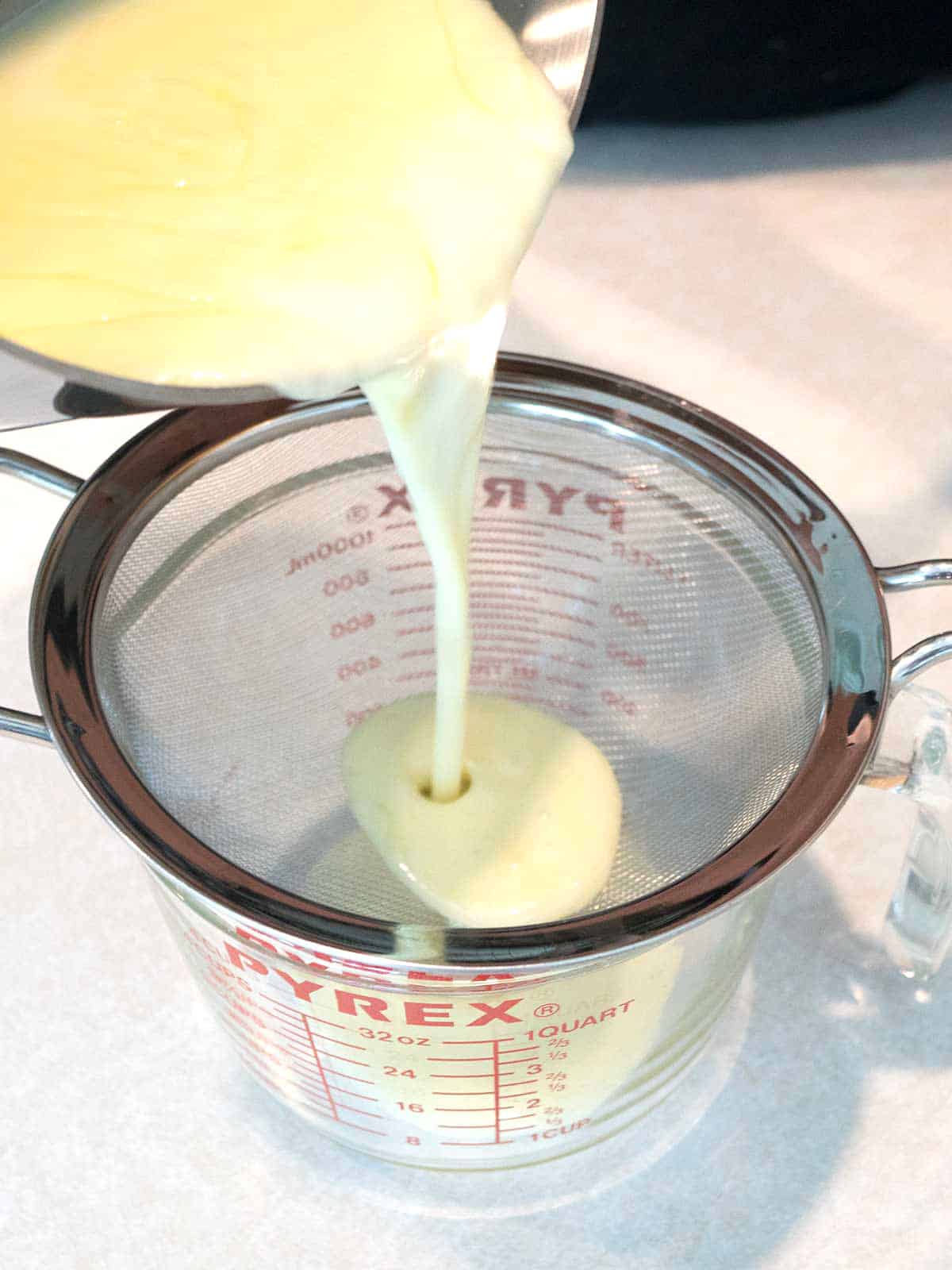 Pouring Posset mixture into a wire mesh strainer to remove the bits of lemon zest.
