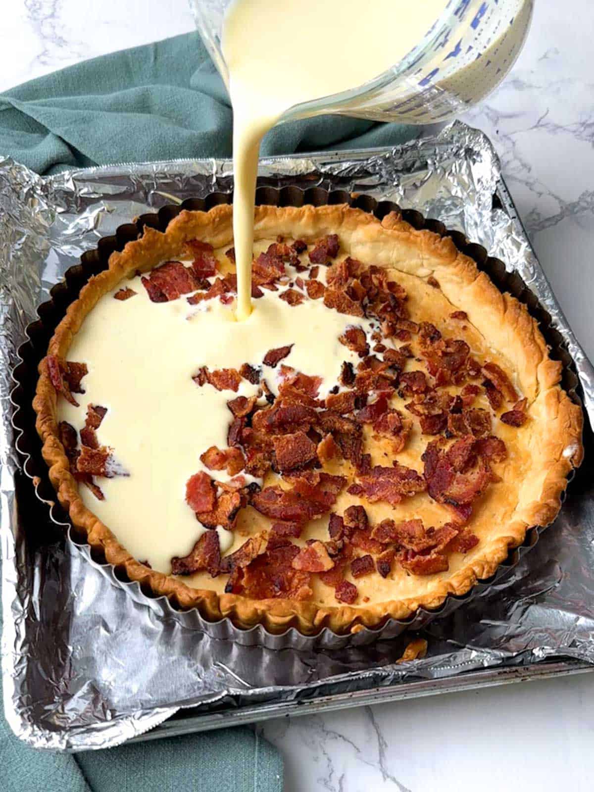 Adding custard to bacon in a pie shell for Quiche Lorraine.