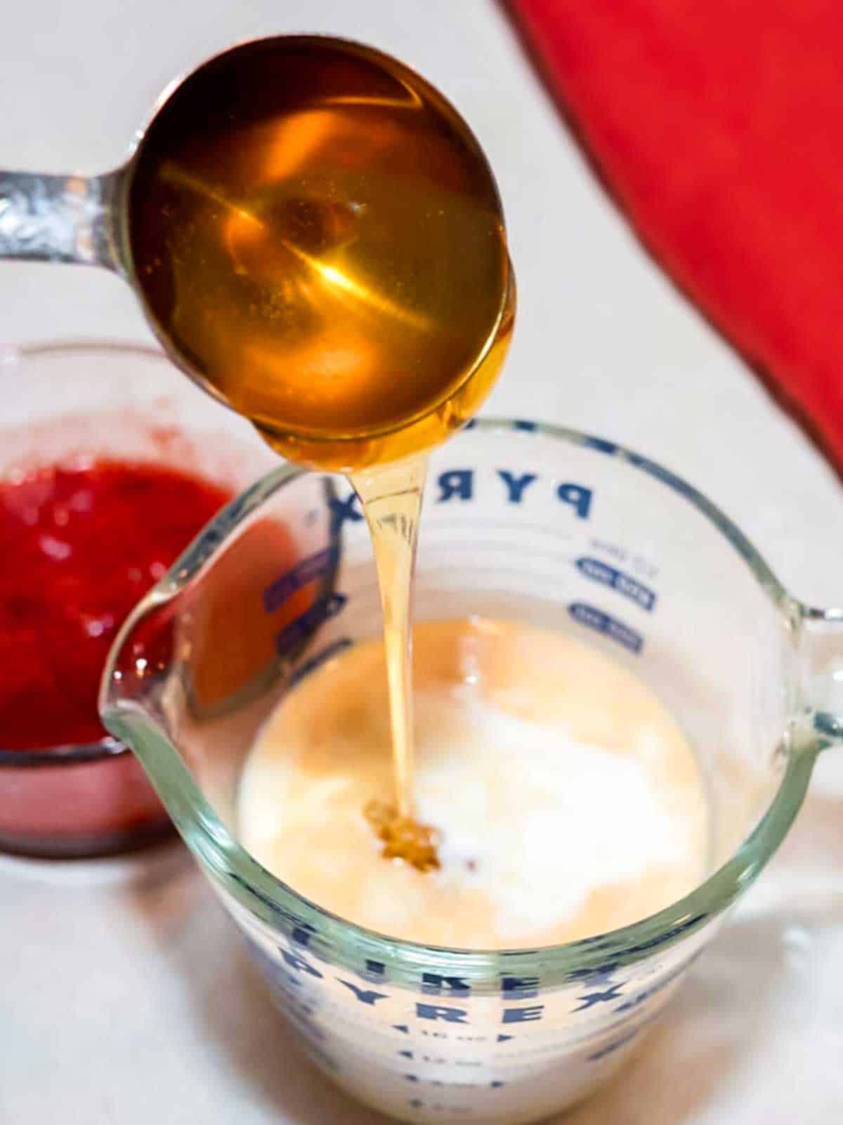 Adding honey to the yogurt, milk, lemon juice and vanilla extract in a measuring cup.
