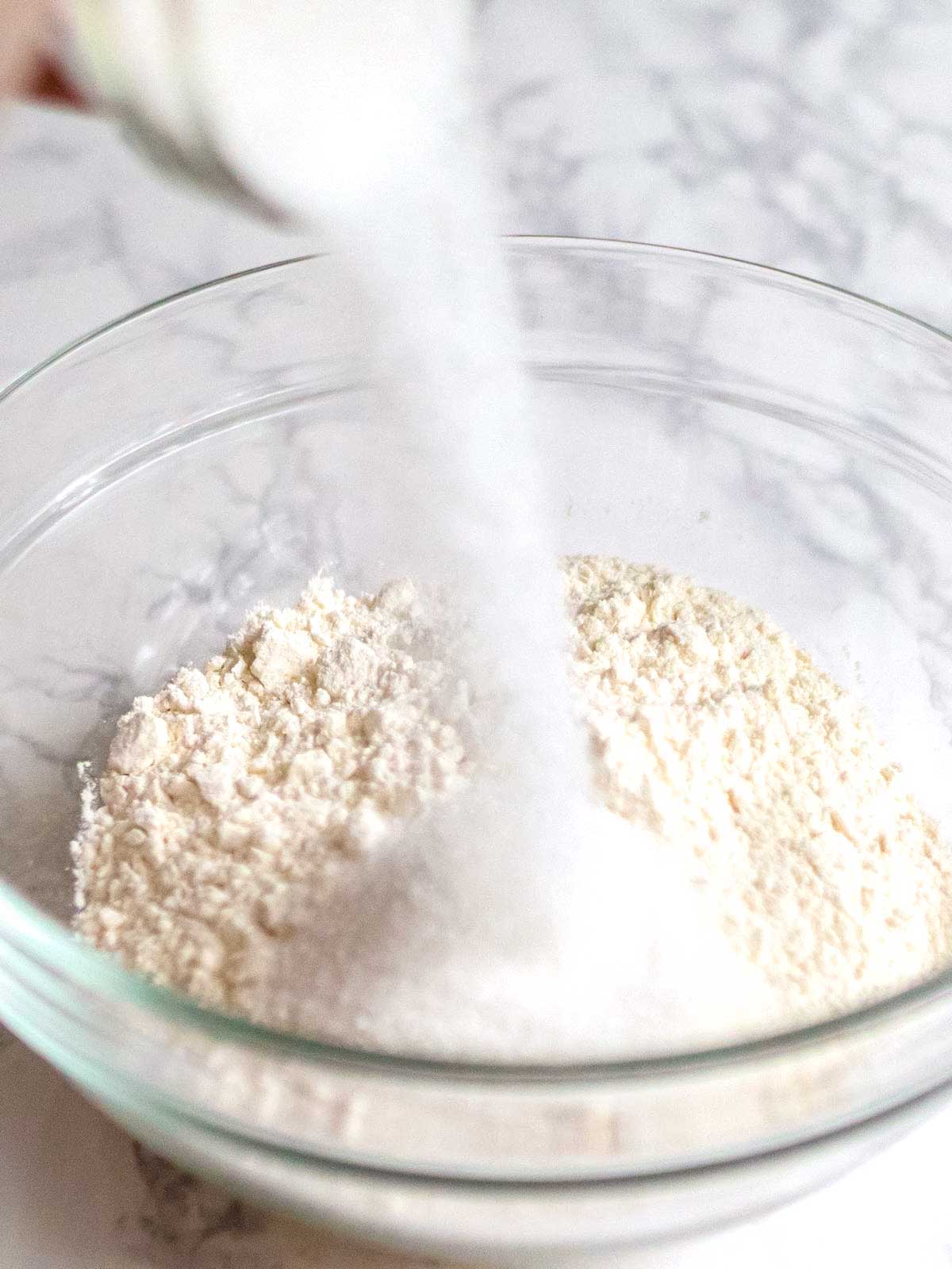 Adding sugar to flour in a bowl.