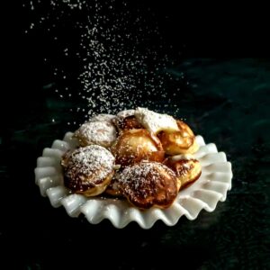 Sprinkling confectioners' sugar on the poffertjes.