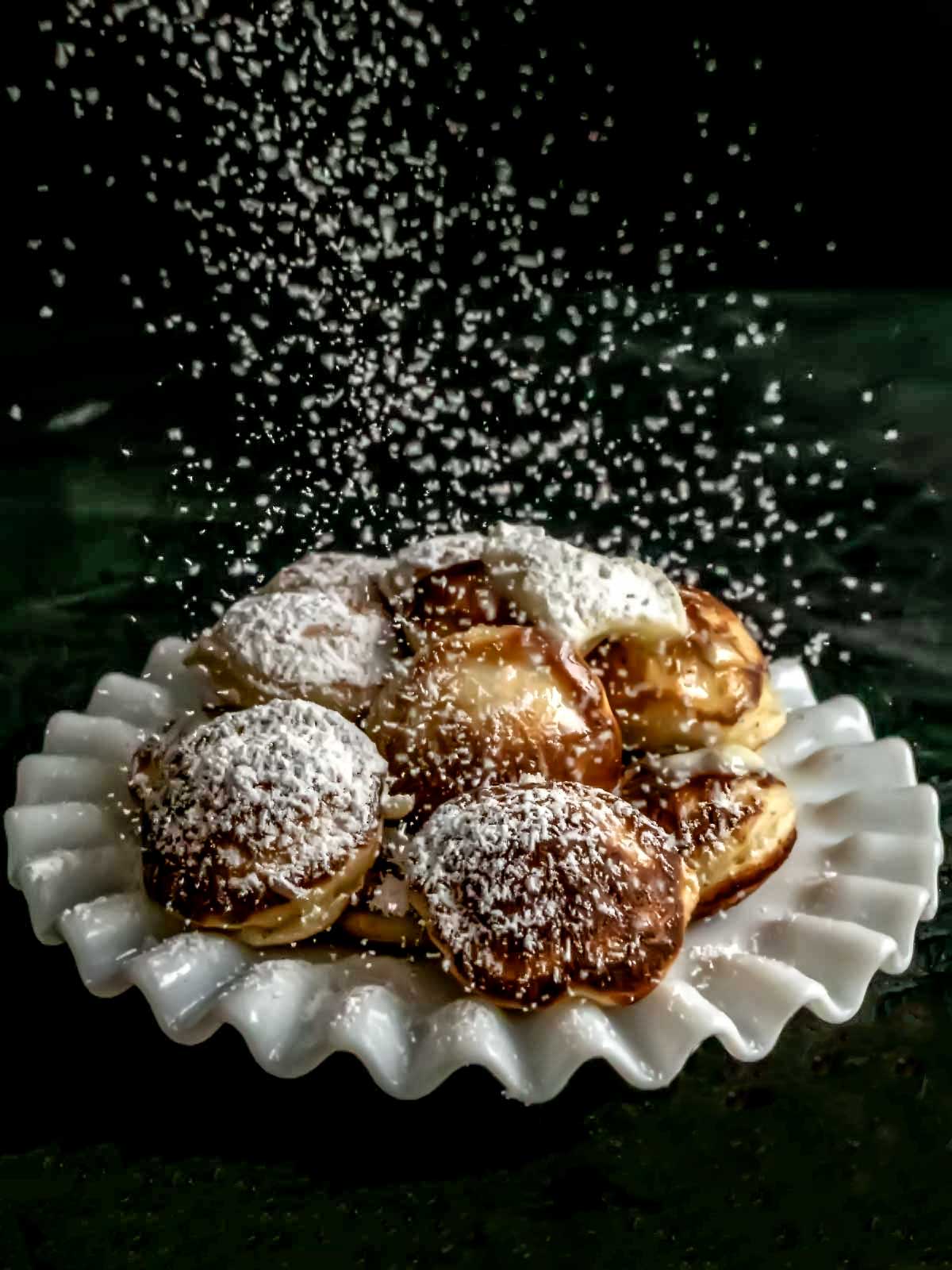 Sprinkling confectioners' sugar on the poffertjes.