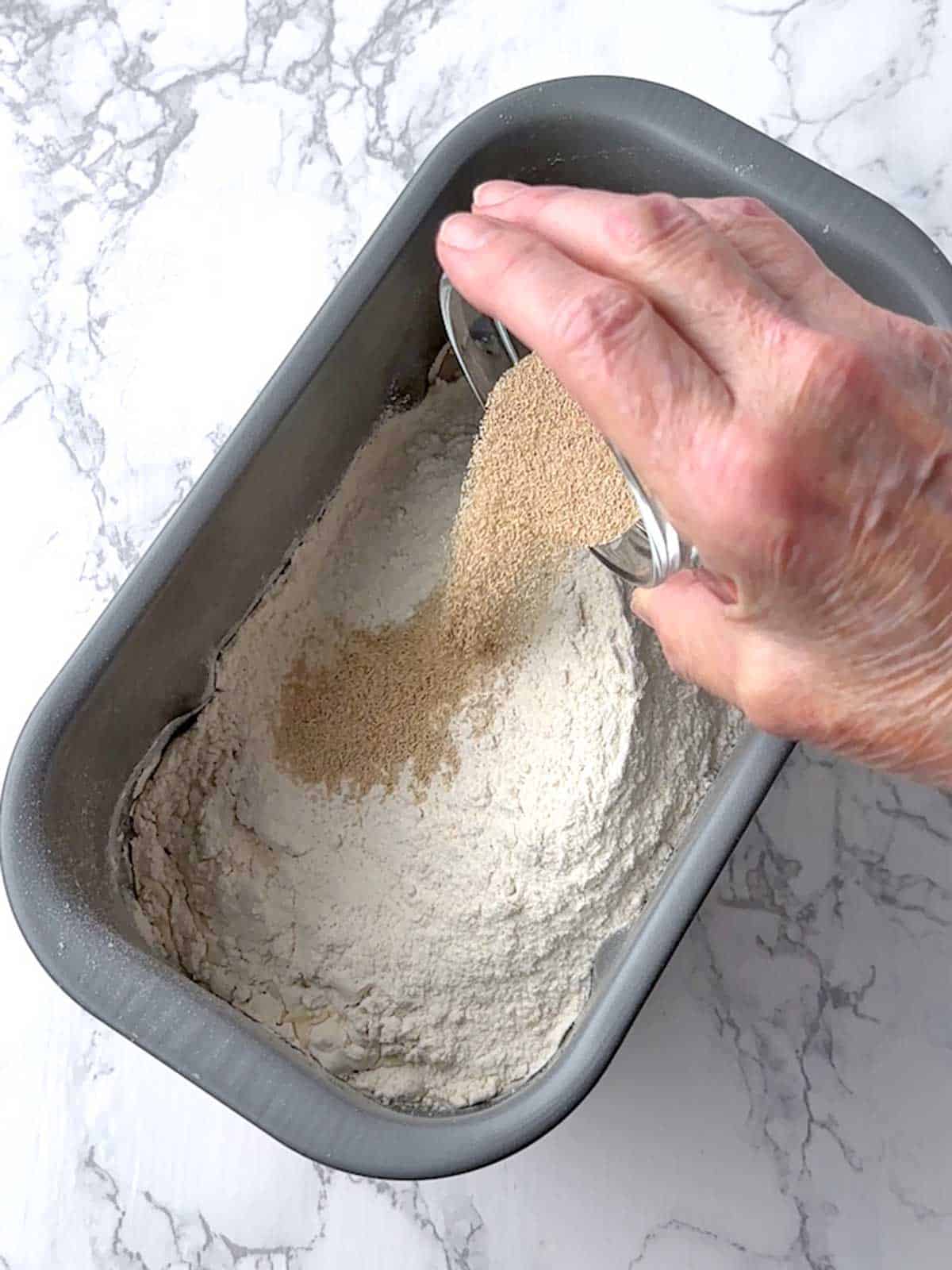 Adding yeast to the bread machine with the other ingredients.