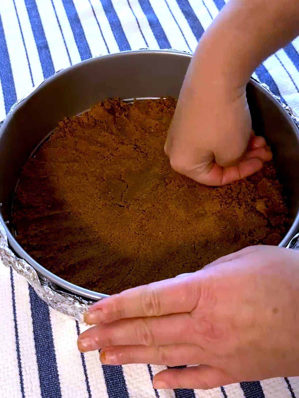 Pressing gingerbread cookie crust into the bottom of a springform pan.