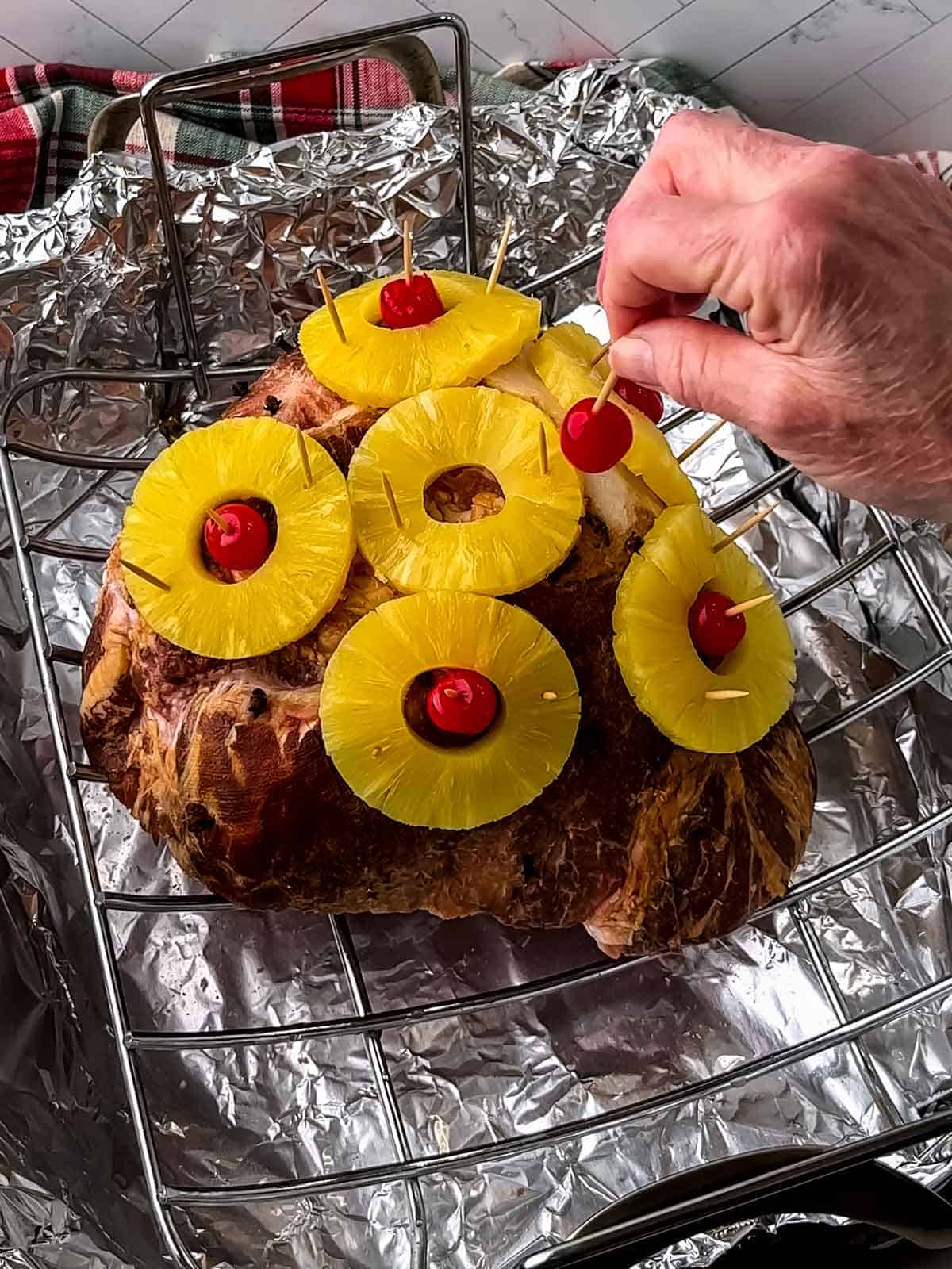 Placing a cherry in the center of a pineapple ring on the ham.