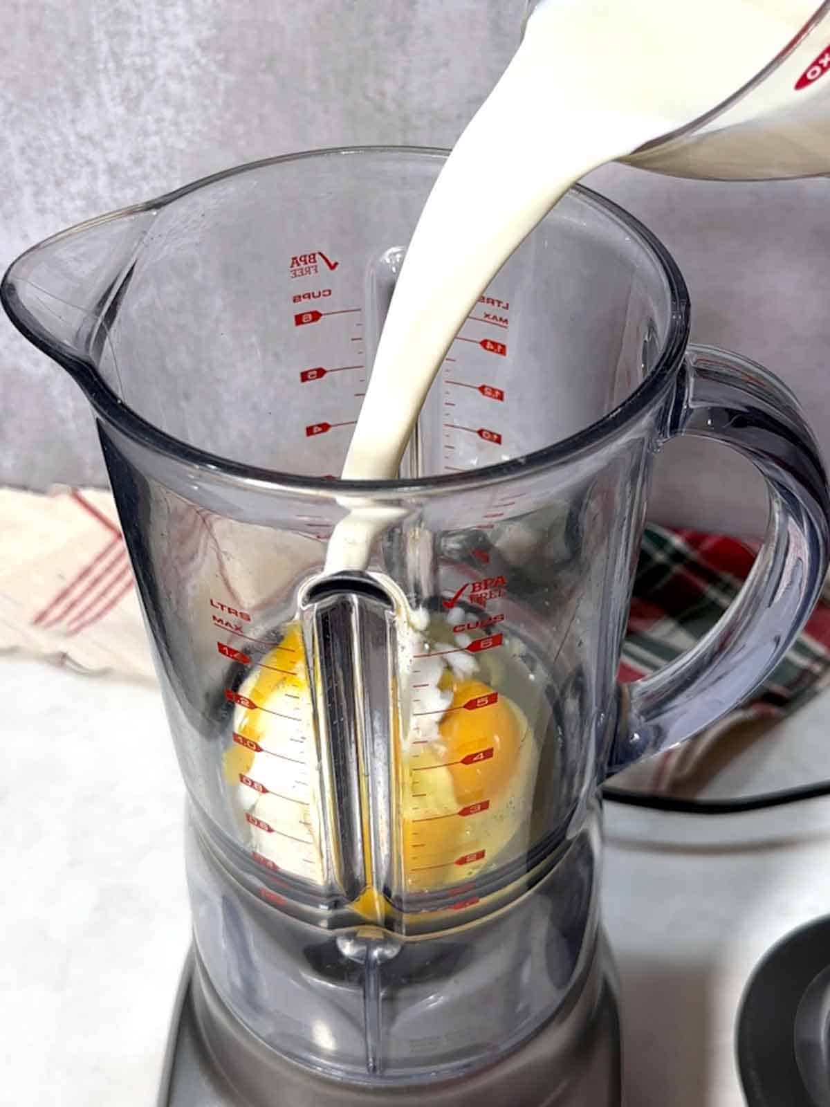 Adding milk to a blender with eggs.