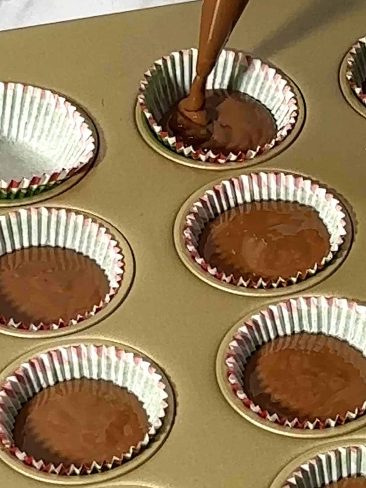 Piping the chocolate peanut butter mixture into the cups of my mini muffin pan.