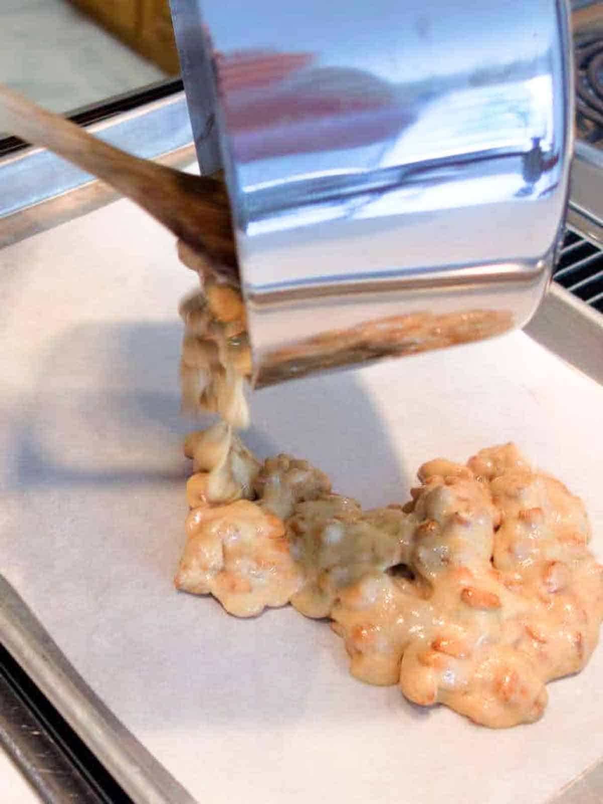 Pouring the peanut brittle on a heated parchment likned baking sheet.