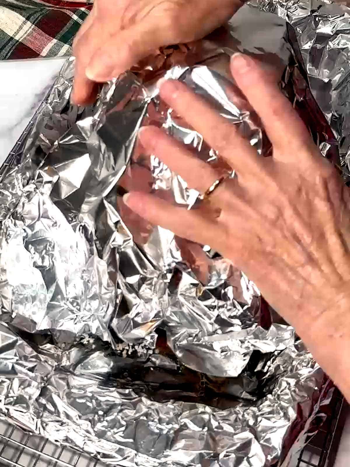 Tenting the cooked roast with aluminum foil.