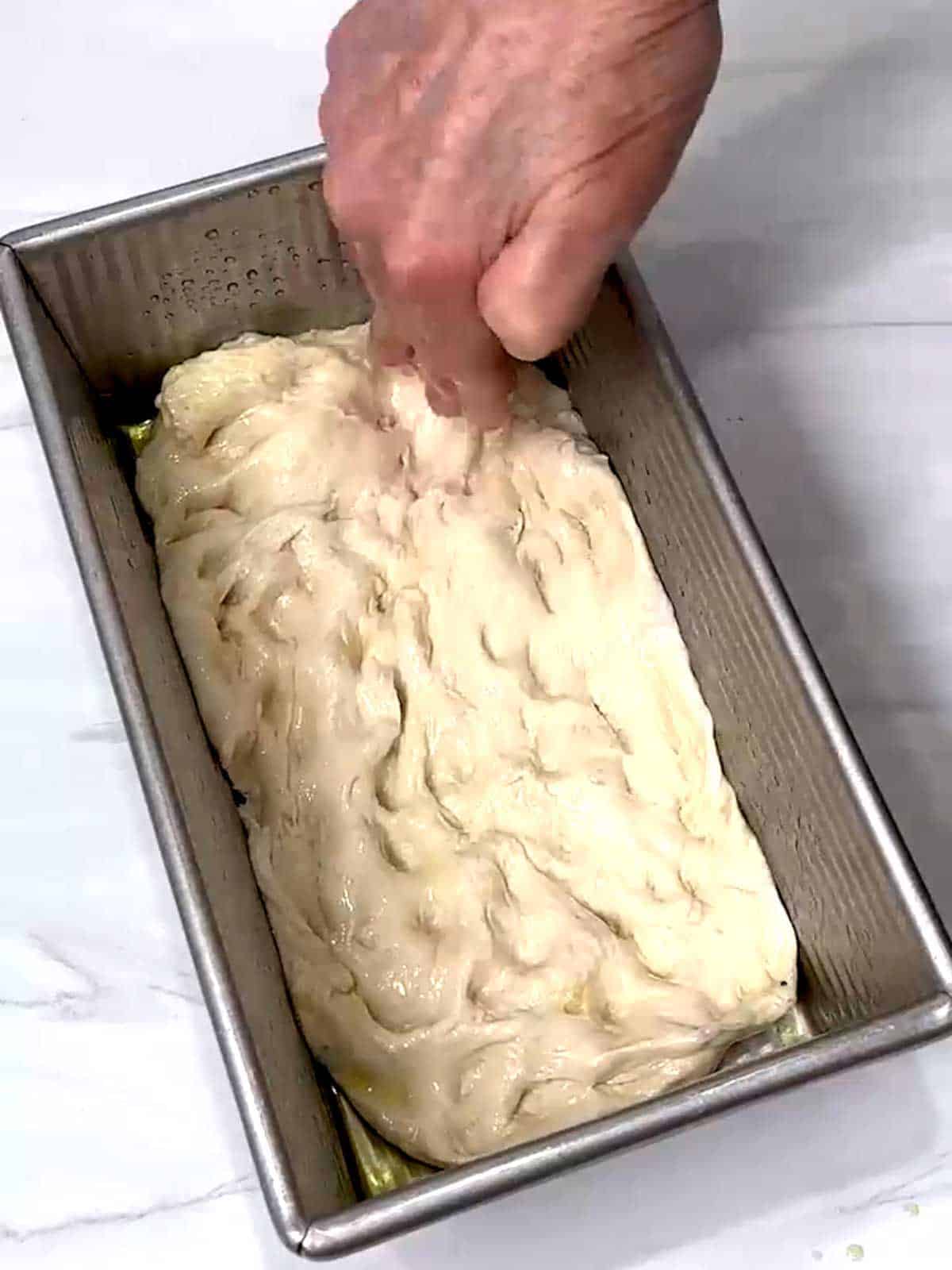 Using fingertips to dimple and stretch the dough in the loaf pan.