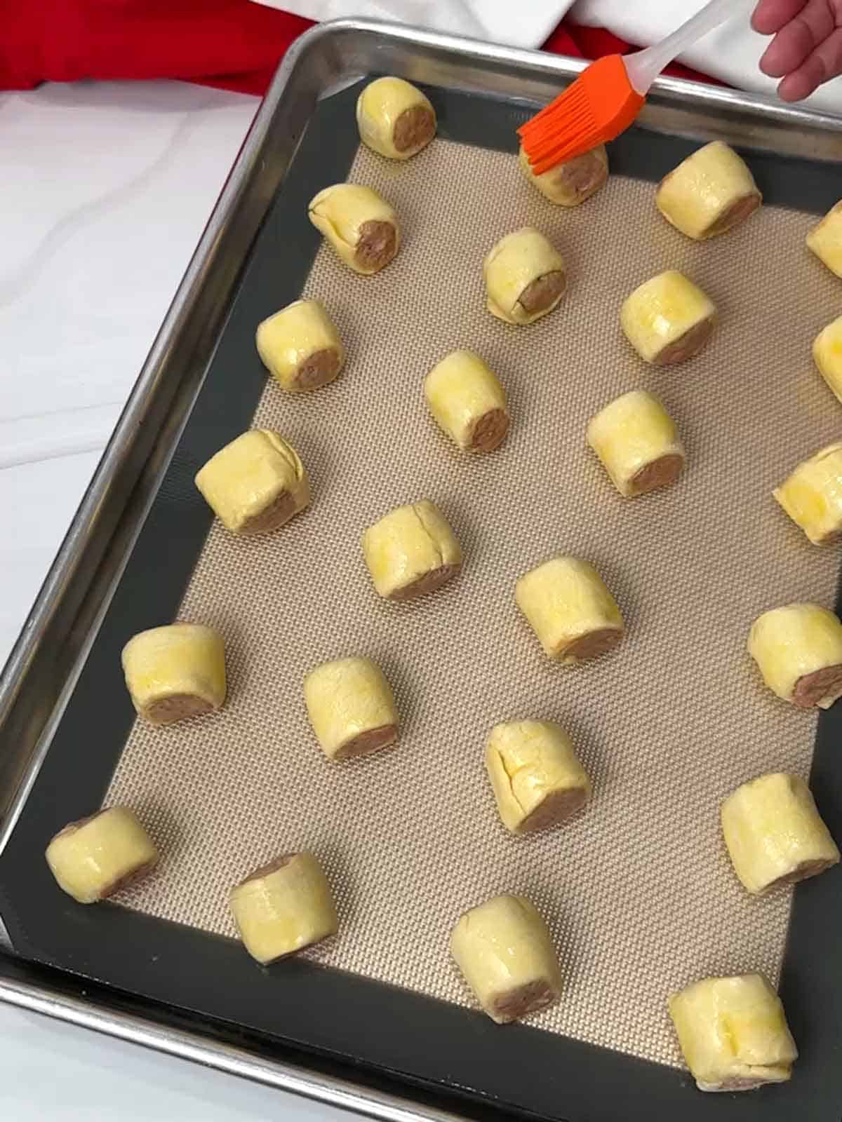 Brushing the sausage roll bites with egg wash.
