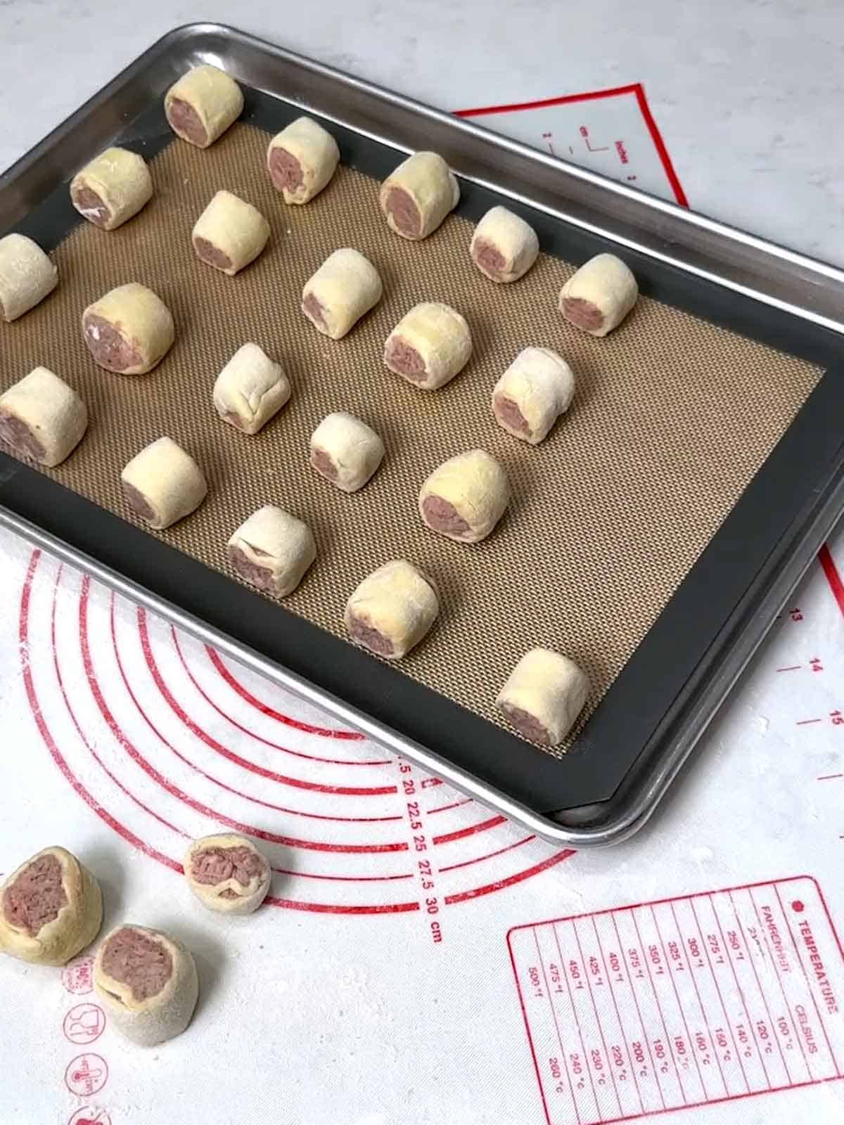 Sausage roll bites on silicone-lined baking sheet.