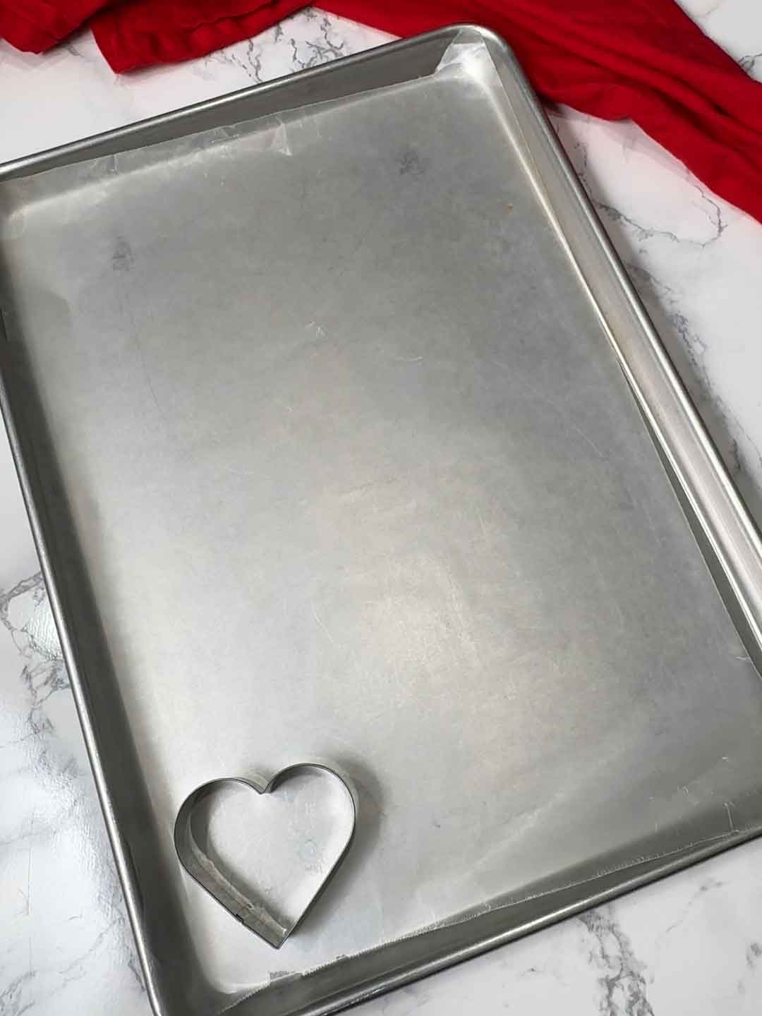 hearts shaped cookie cutter on wax paper lined baking sheet