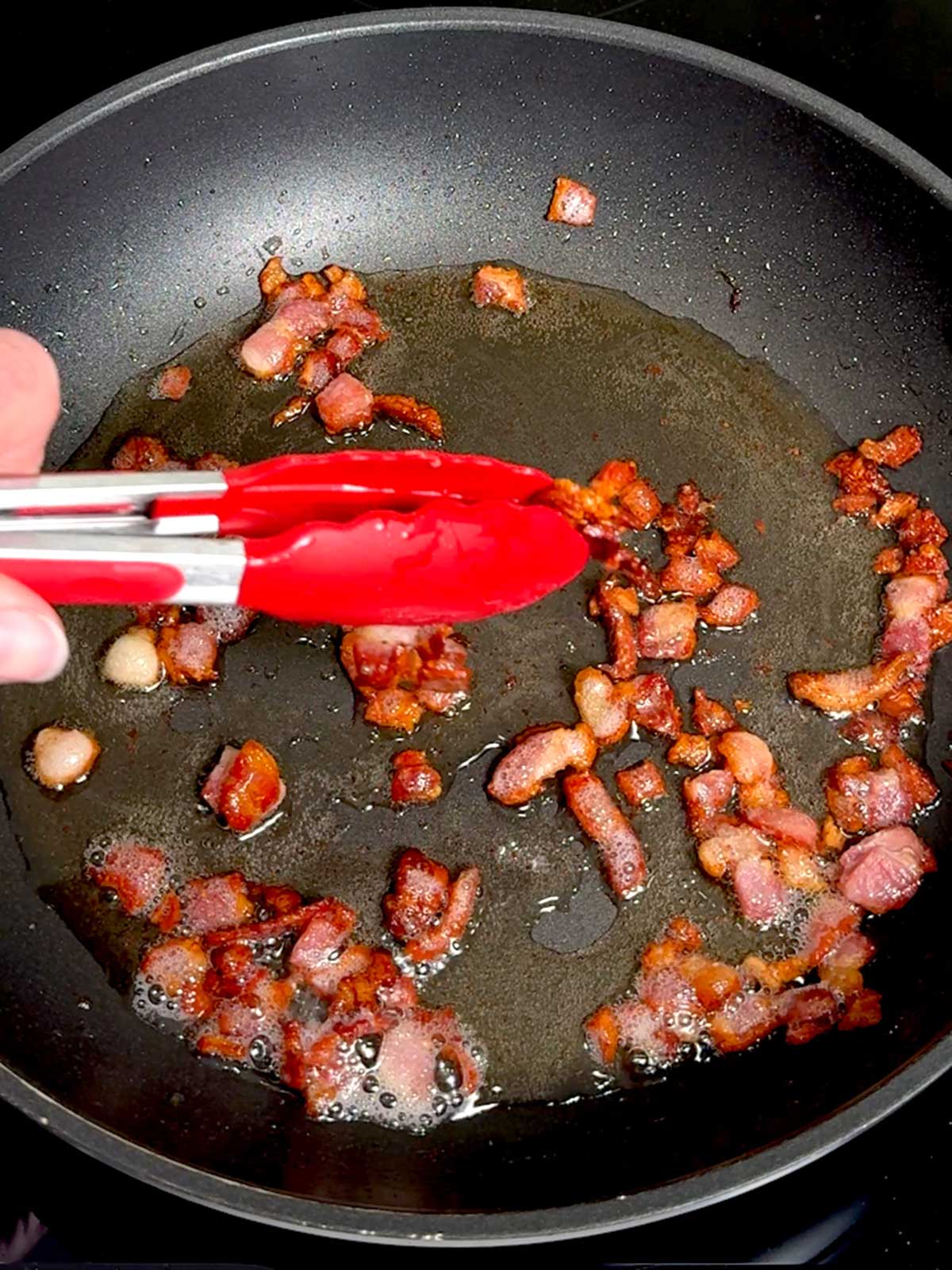 Removing cooked bacon from the skillet to drain.