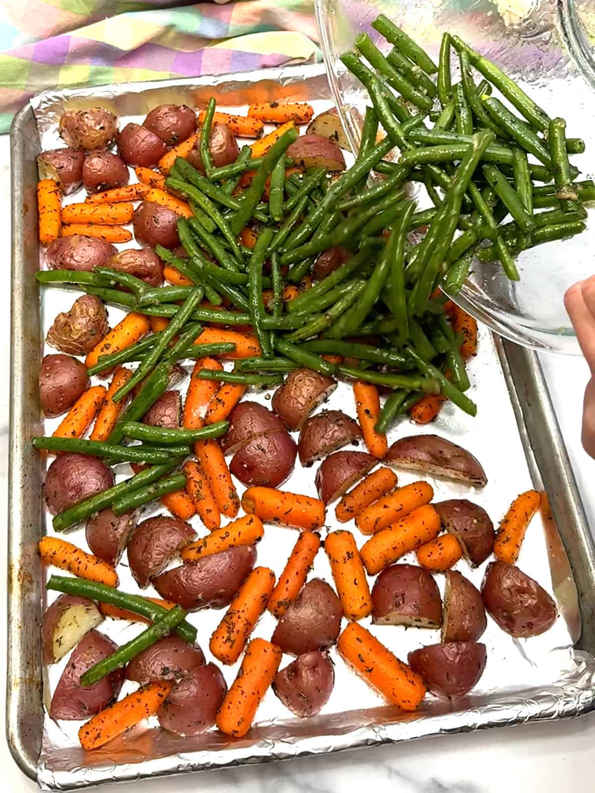 adding green beans to pan with potatoes and carrots