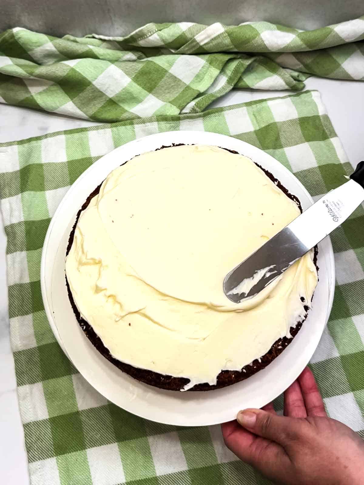 smoothing out frosting on bottom layer of carrot cake