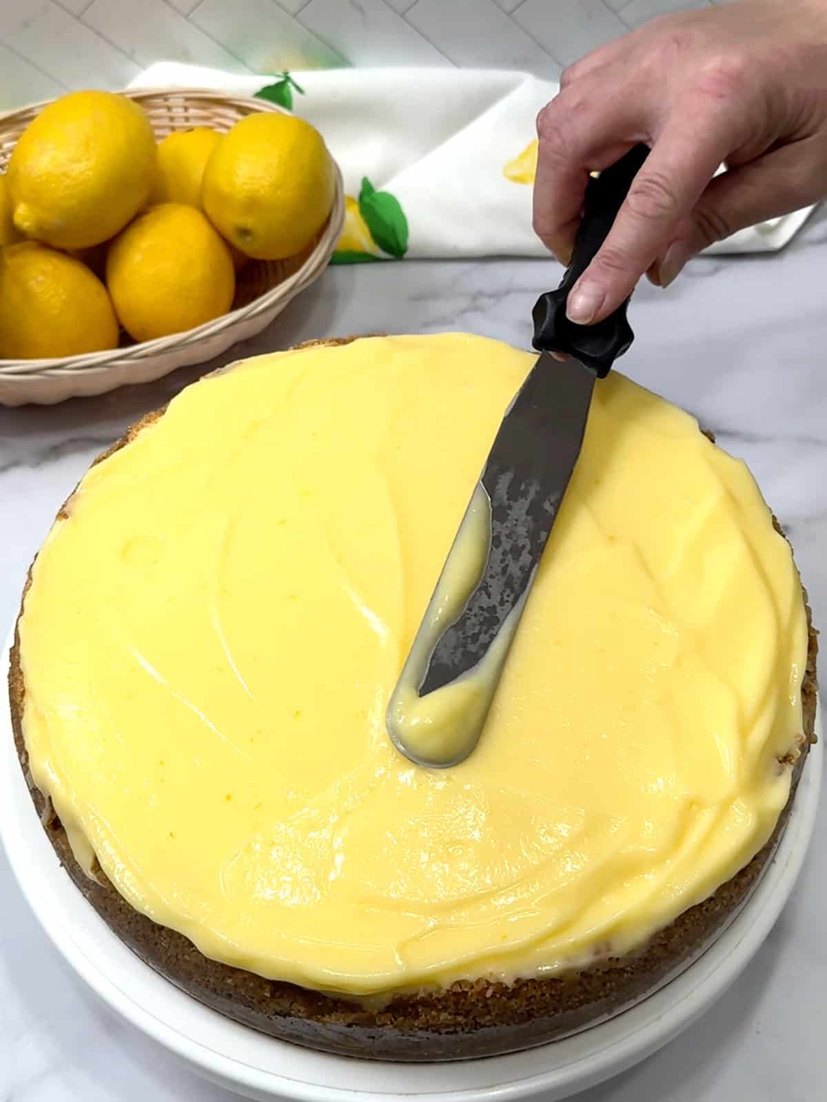 spreading lemon curd on top of cheesecake