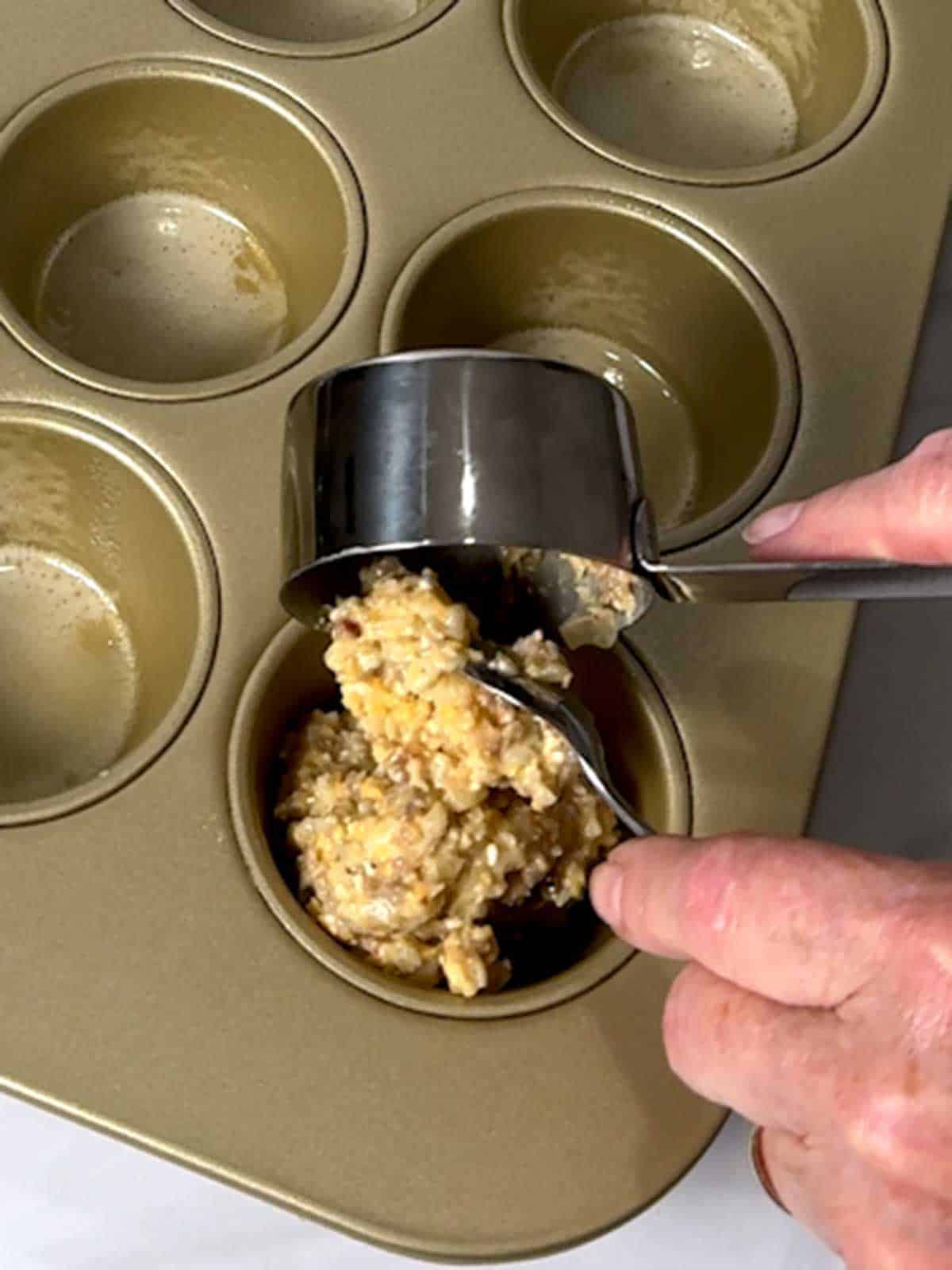 Adding the sausage, egg, cheese, and hash brown mixture to a cavity in a regular muffin pan.