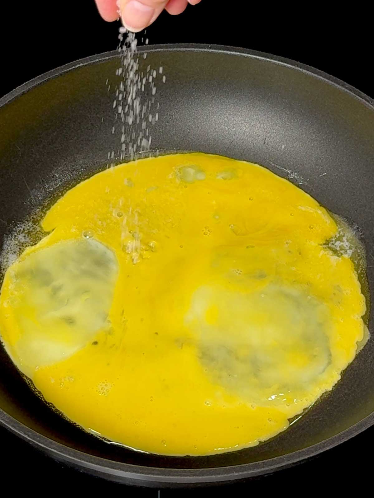 Sprinkling salt on eggs in the skillet.