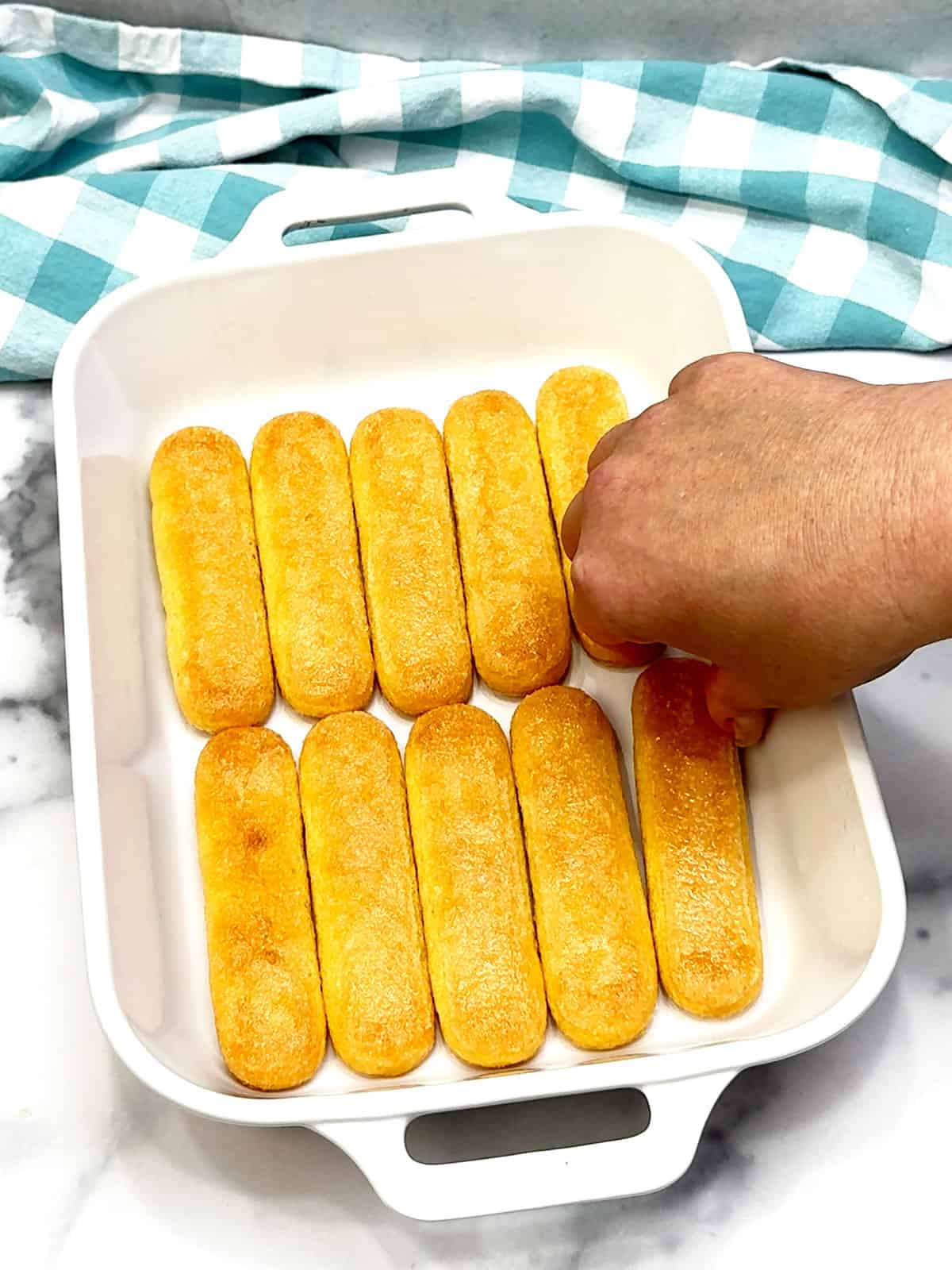 placing dipped ladyfingers in bottom of pan