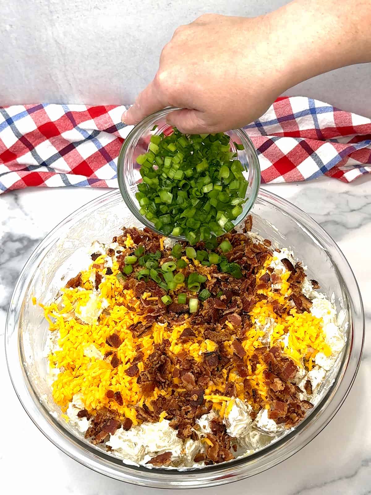 adding cheddar cheese, crumbled bacon, and green onions to potatoes