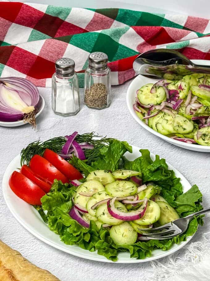 Cucumber dill salad on a plate with tomato, dill and onions.