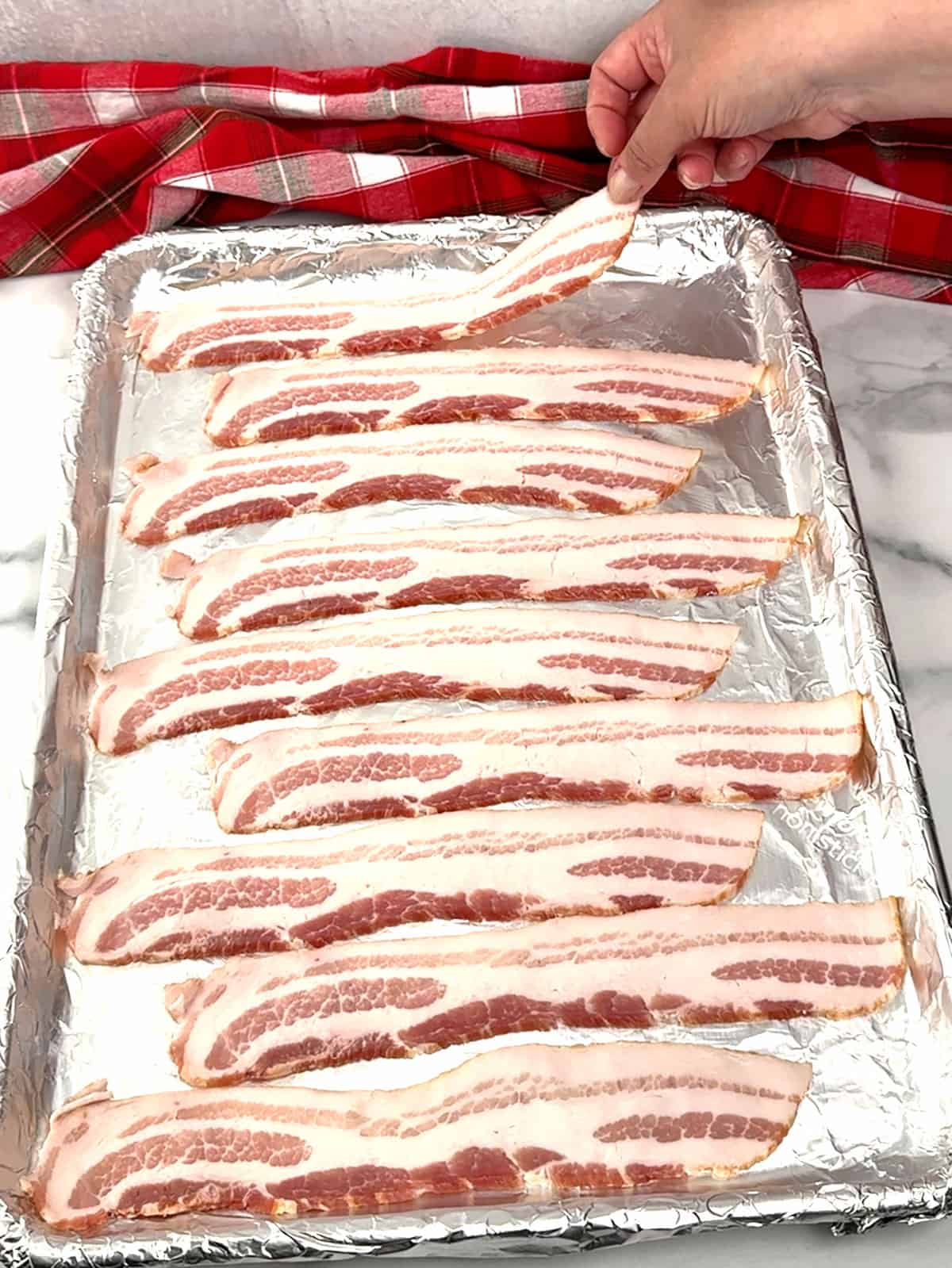 placing uncooked bacon on prepared sheet pan 