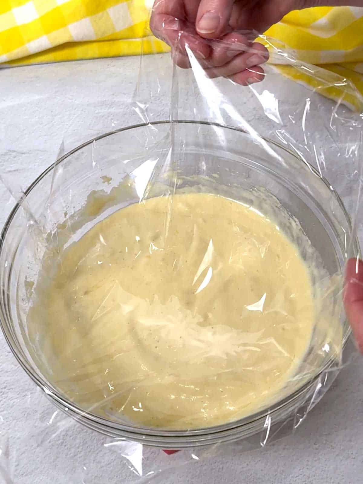 Placing a piece of plastic wrap on the surface of the madeleine batter.