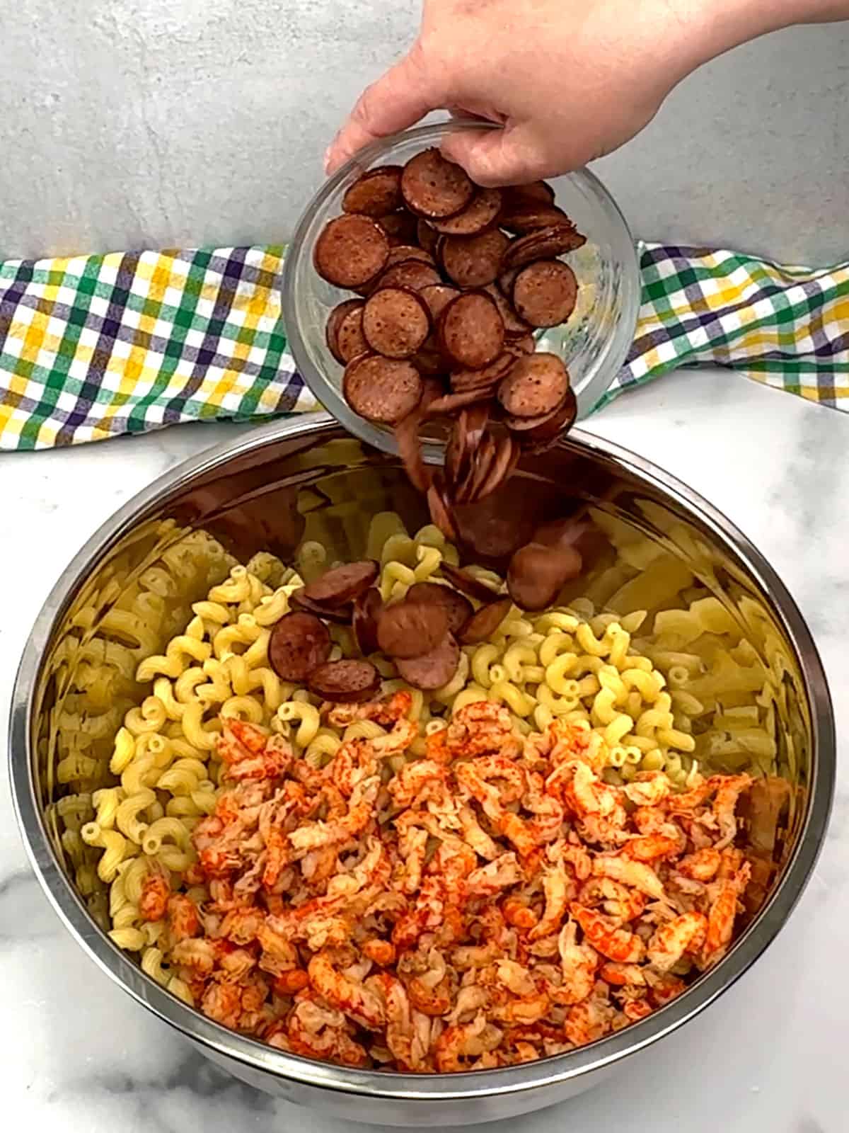 adding pasta, sausage and crawfish to a large bowl