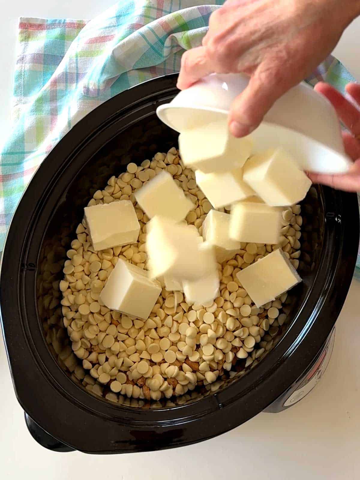 Adding the almond bark to the crockpot with the peanuts and white chips.