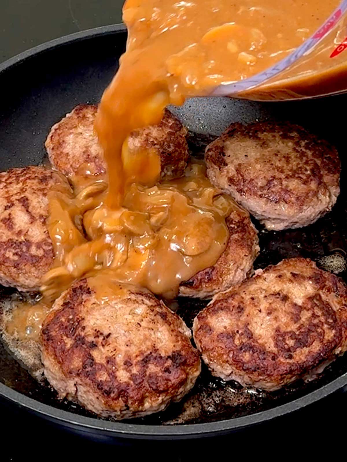 Adding the gravy to the Salisbury steak in the pan.