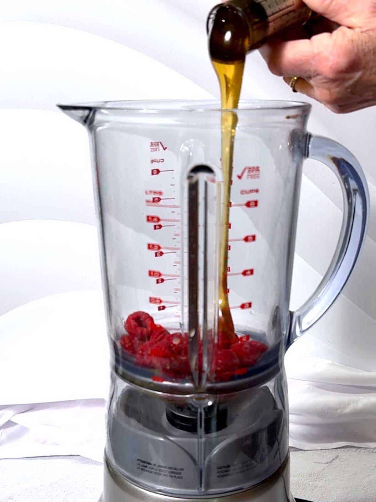 Adding honey to the raspberries in the blender.