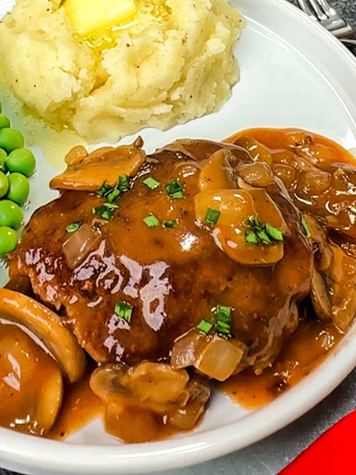 Classic Salisbury Steak with mashed potatoes and green peas.