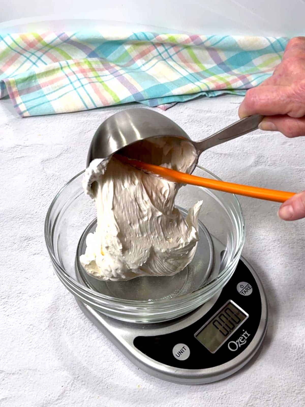Transferring cheesecake mixture to a bowl on a kitchen scale.