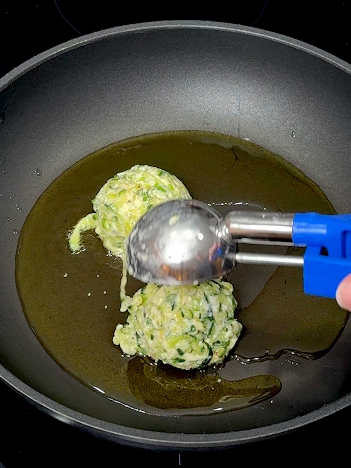 Adding the fritter batter to the pan using a large ice cream scoop.