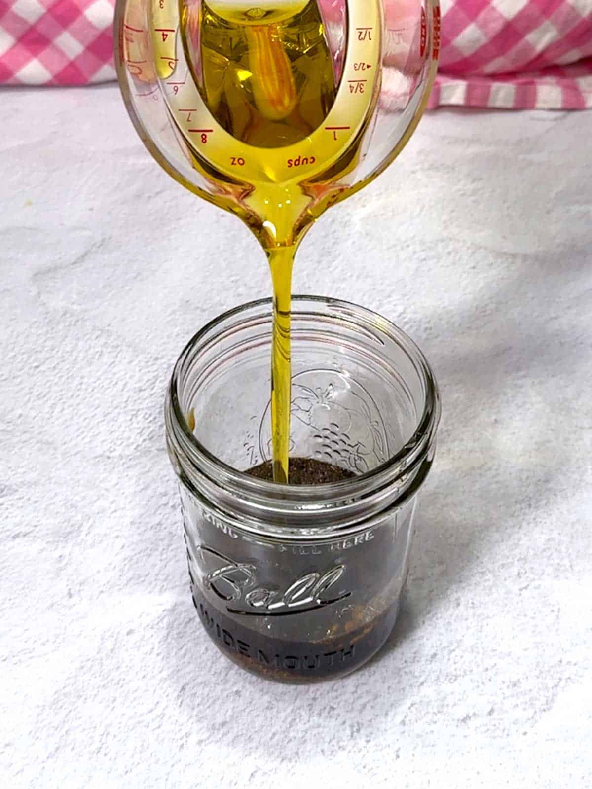 Adding olive oil to remaining vinaigrette ingredients in a jar.