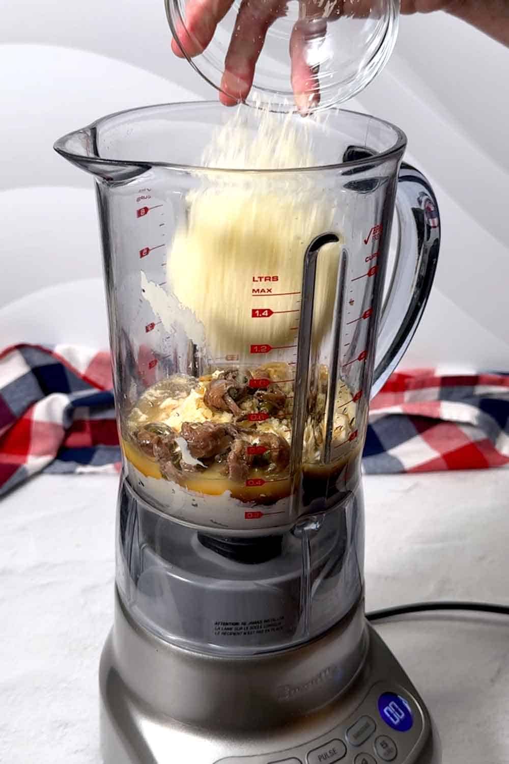 Adding Parmesan cheese to a blender with other dressing ingredients.