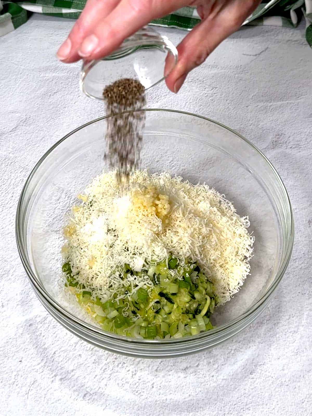 Adding black pepper to the fritter ingredients in a medium bowl.