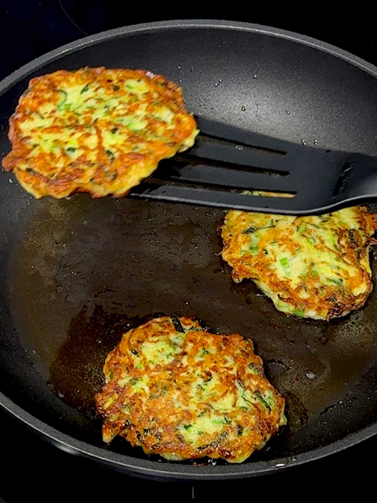 Removing the zucchini fritters from the pan.