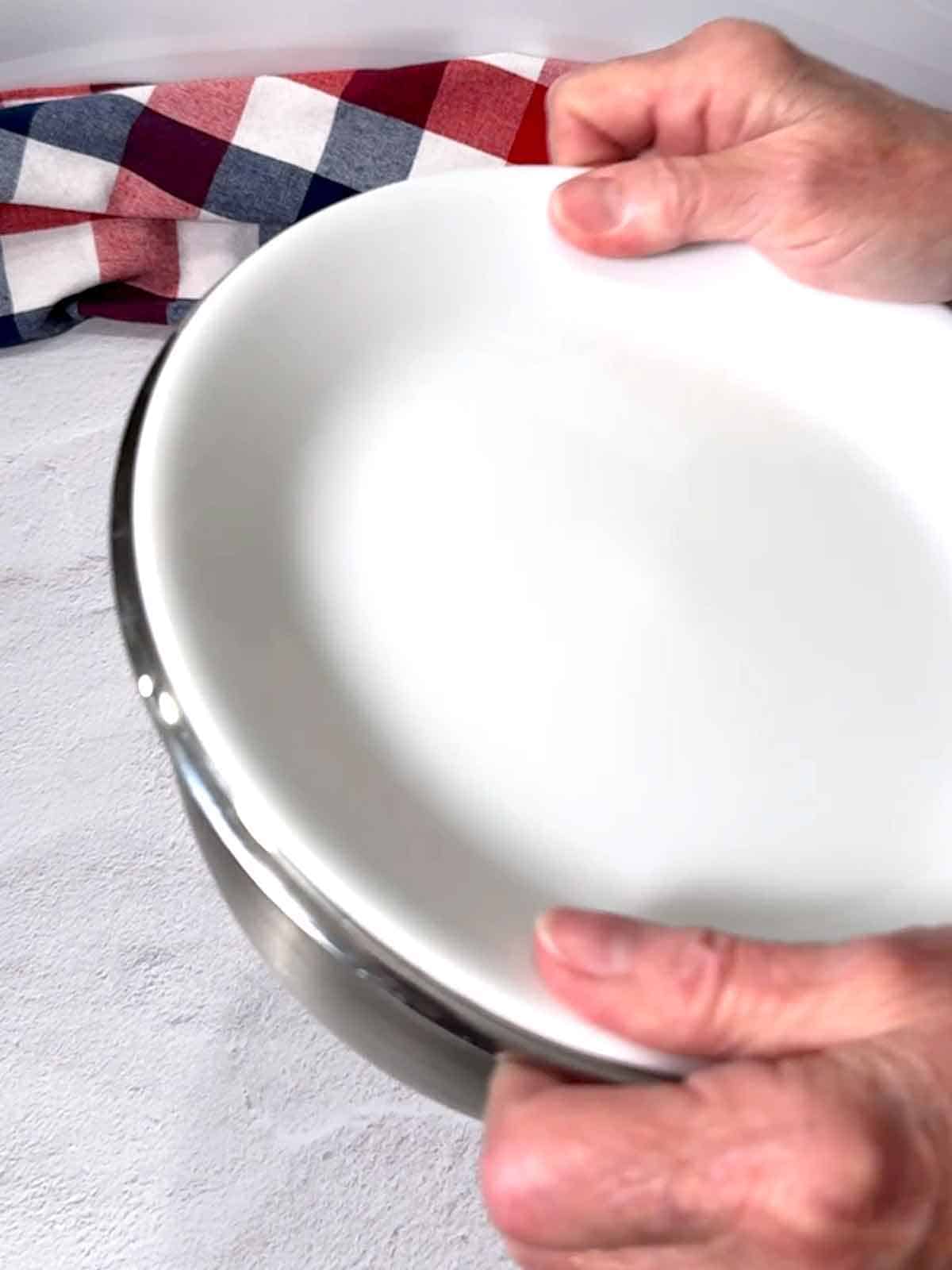 Shaking the crouton ingredients with a plate on top of the bowl.
