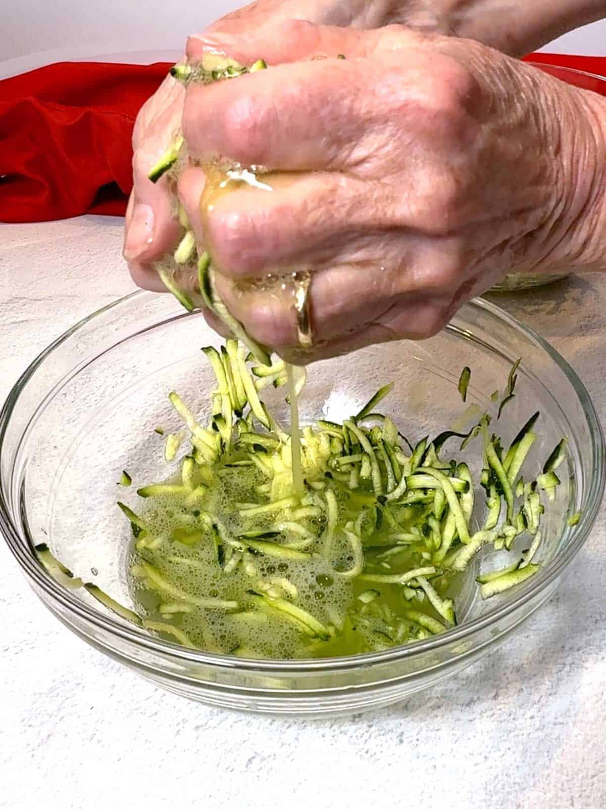 Squeezing handfuls of zucchini to remove excess liquid.