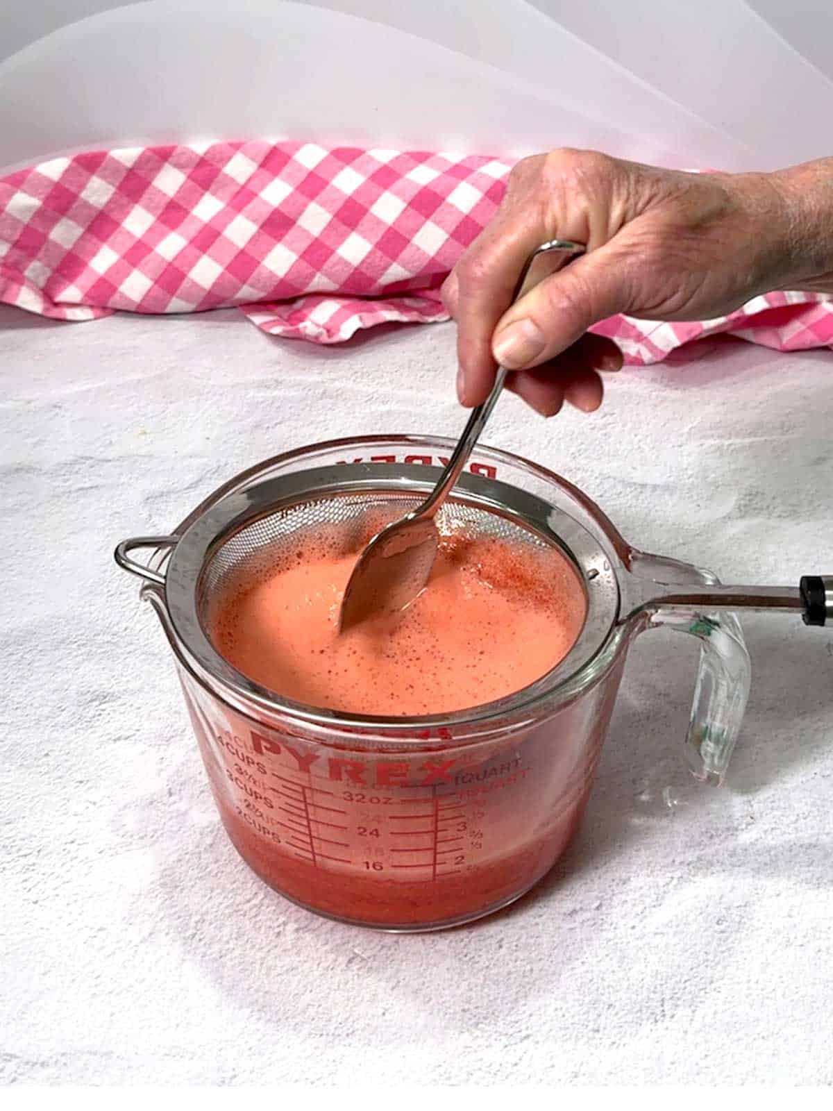 Stirring the mixture to remove bits of strawberries.