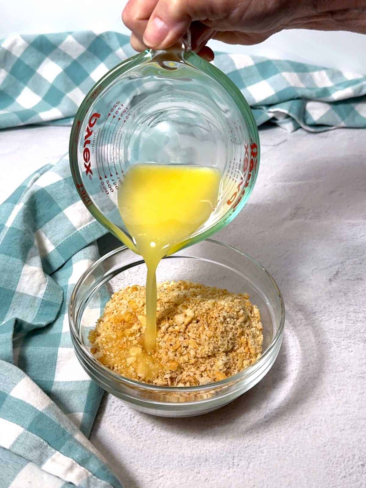 Adding melted butter to Ritz Cracker crumbs in a bowl.