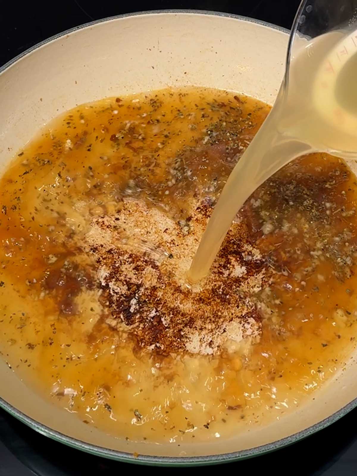 Adding chicken broth to the braiser.