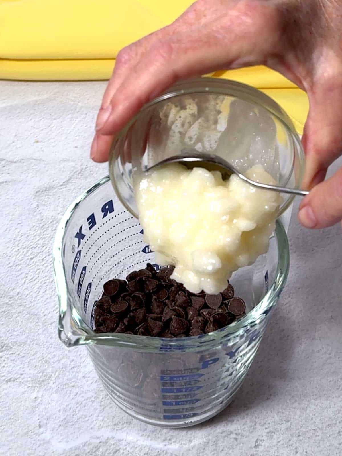 Adding coconut oil to chocolate chips in a measuring cup.