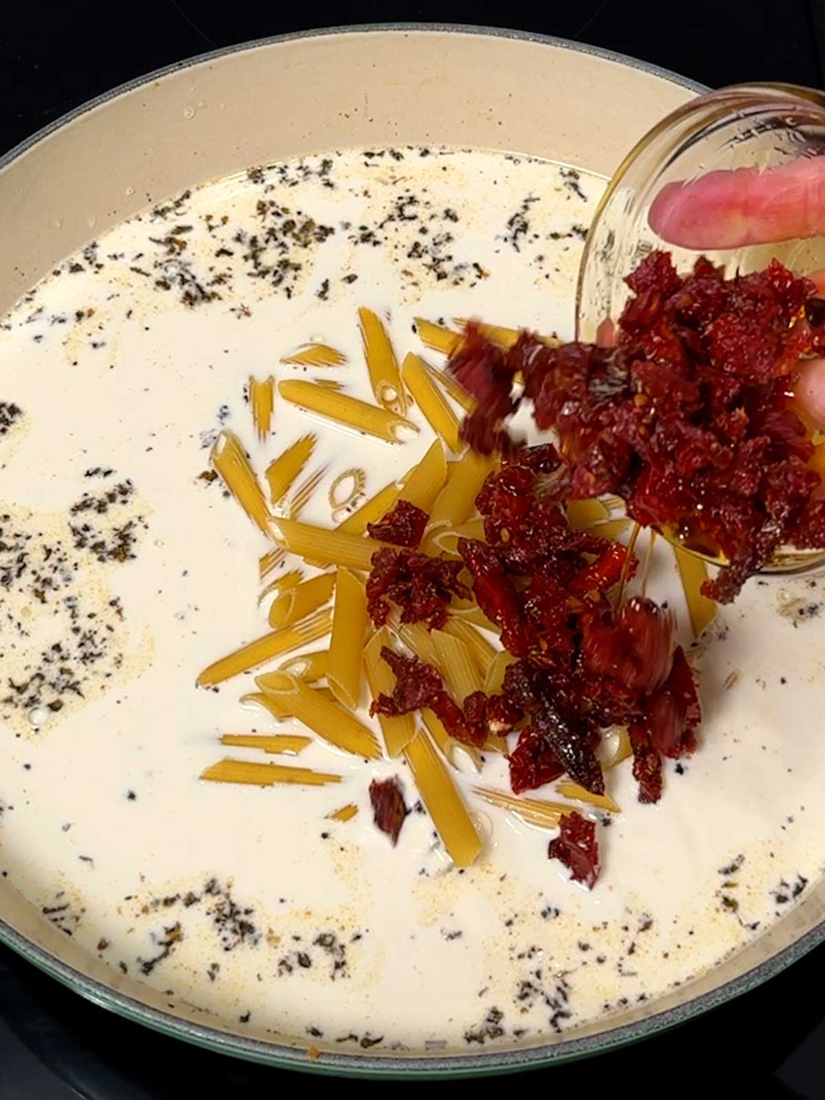 Adding sun-dried tomatoes to the braiser along with dry penne.