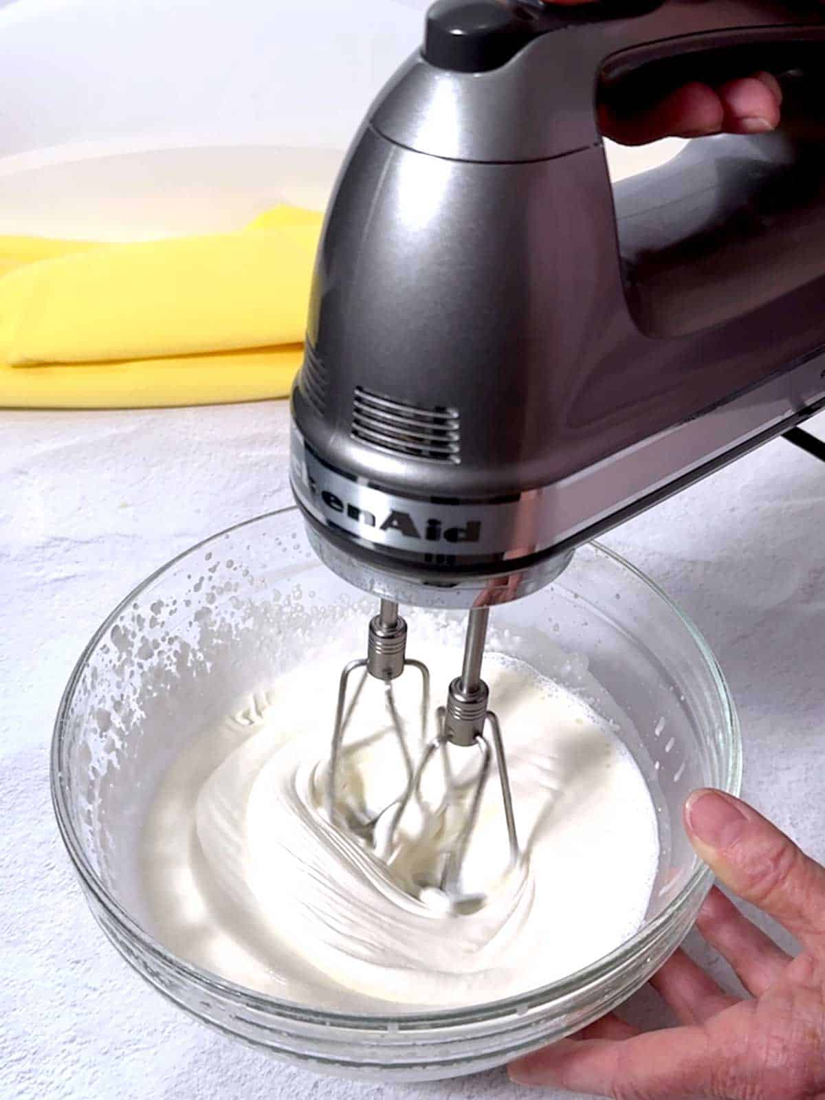 Beating the cream with an electric mixer.