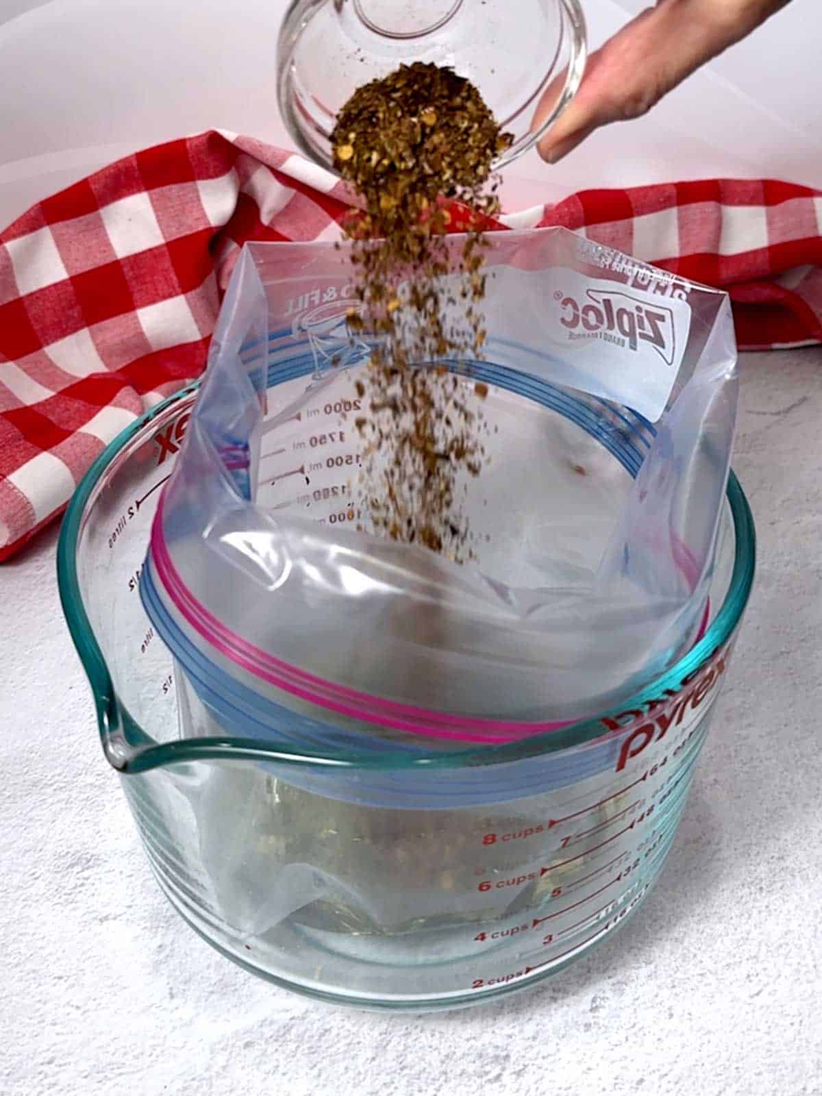 Adding crushed chile peppers to the ZipLoc bag with the other ingredients.