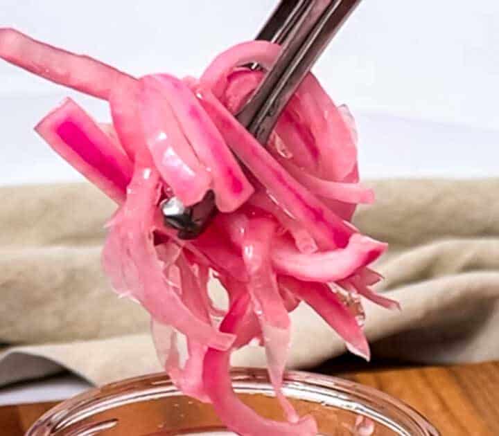 Pickled red onions held by tongs.